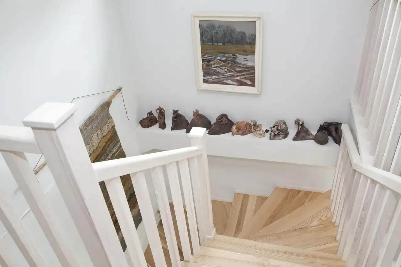 Klatka schodowa inspiracje: drewniane stopnie, białe balustrady i galeria ceramicznych rzeźb tworzą artystyczną przestrzeń.