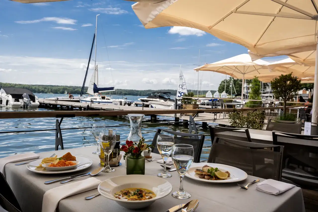 Elegancko nakryty stolik z daniami i widokiem na jezioro z żaglówkami. Idealne miejsce na obiad w najlepszej restauracji w Olsztynie.