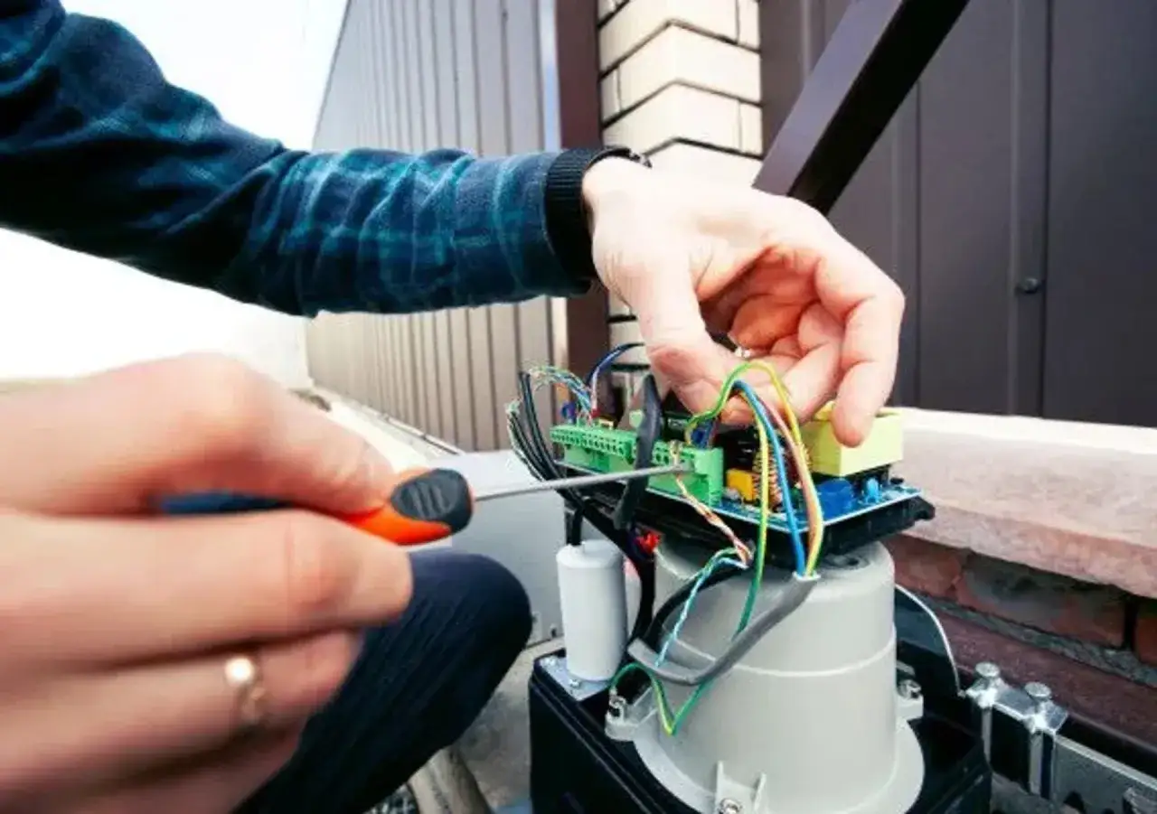 R&eacute;paration du circuit d'un portail &eacute;lectrique bloqu&eacute; ouvert. Un tournevis ajuste les fils color&eacute;s.