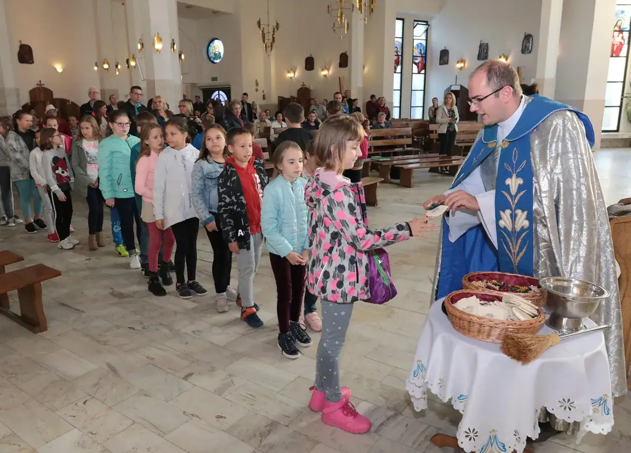 Dzieci w kościele czekają w kolejce do kapłana, który udziela im komunii. Ile trwa różaniec w kościele? Zależy od tego, jak szybko dzieci się ustawią.