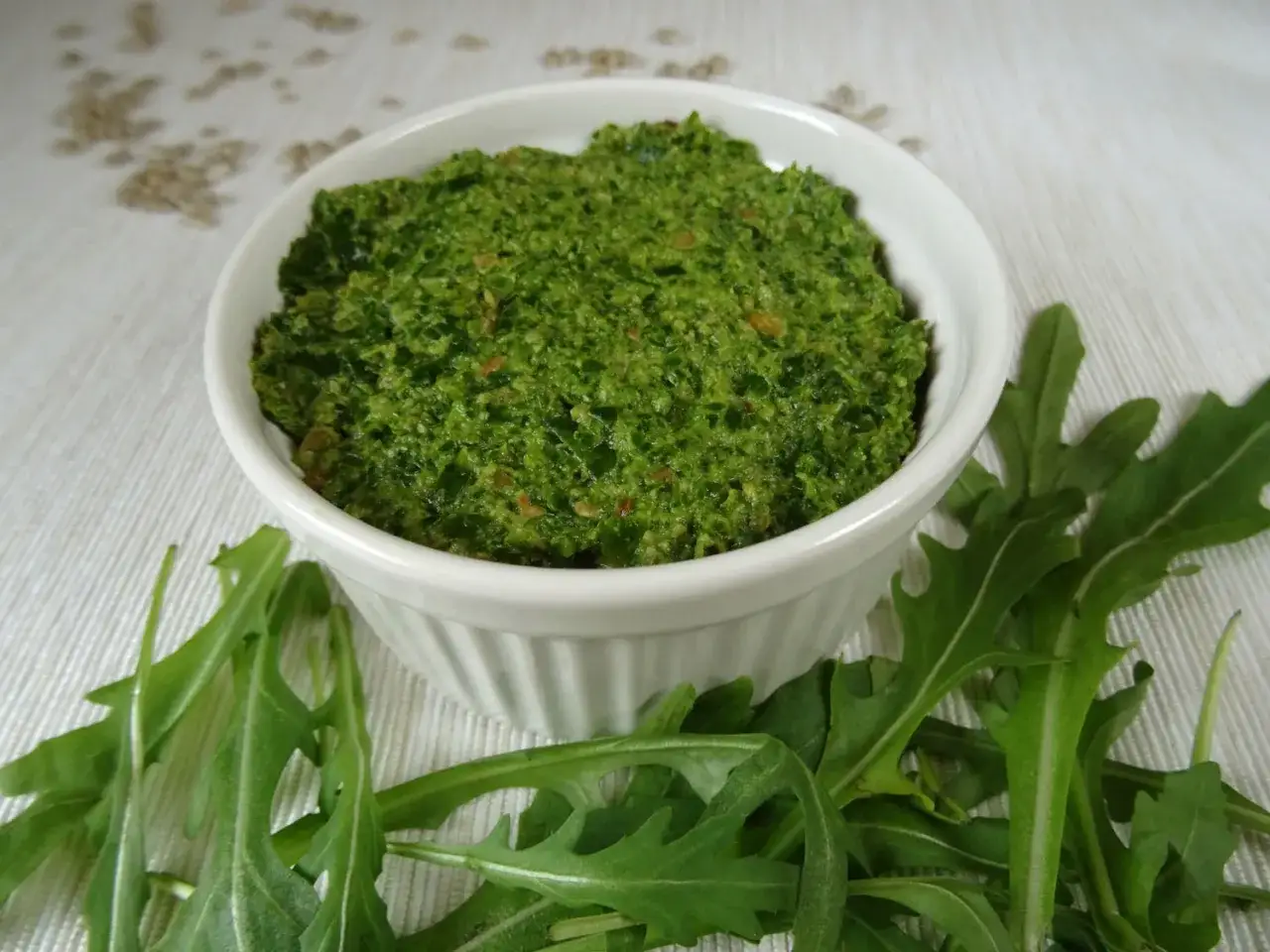 Domowe pesto z rukoli w białej miseczce, otoczone świeżymi liśćmi rukoli. Idealne do makaronu lub na kanapki.