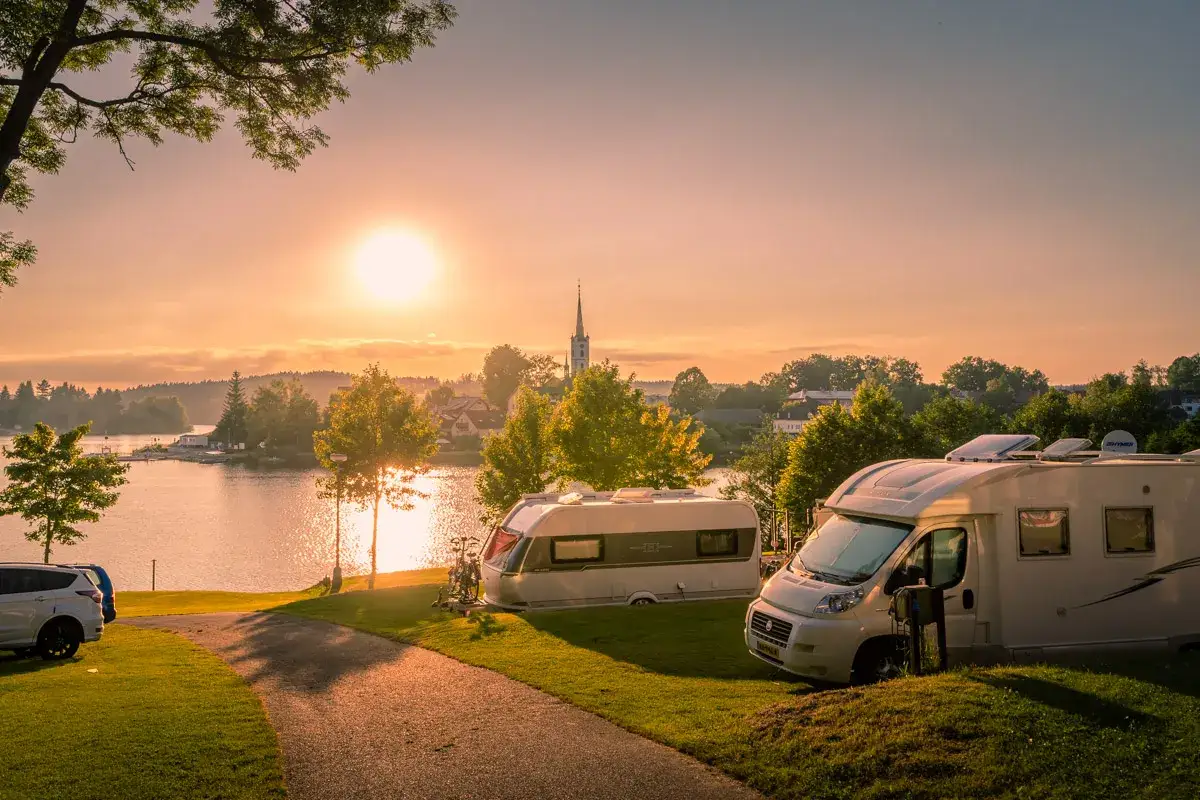 Zachód słońca nad jeziorem, kampery i przyczepy kempingowe na polu namiotowym. Idealne miejsce na **camping Czechy**.
