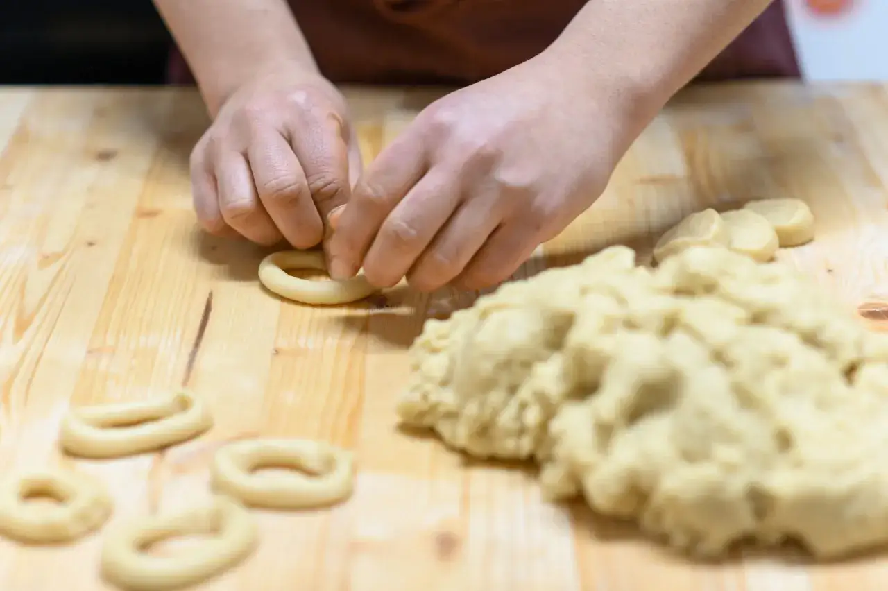 Mani che modellano impasto per creare taralli salati pugliesi.