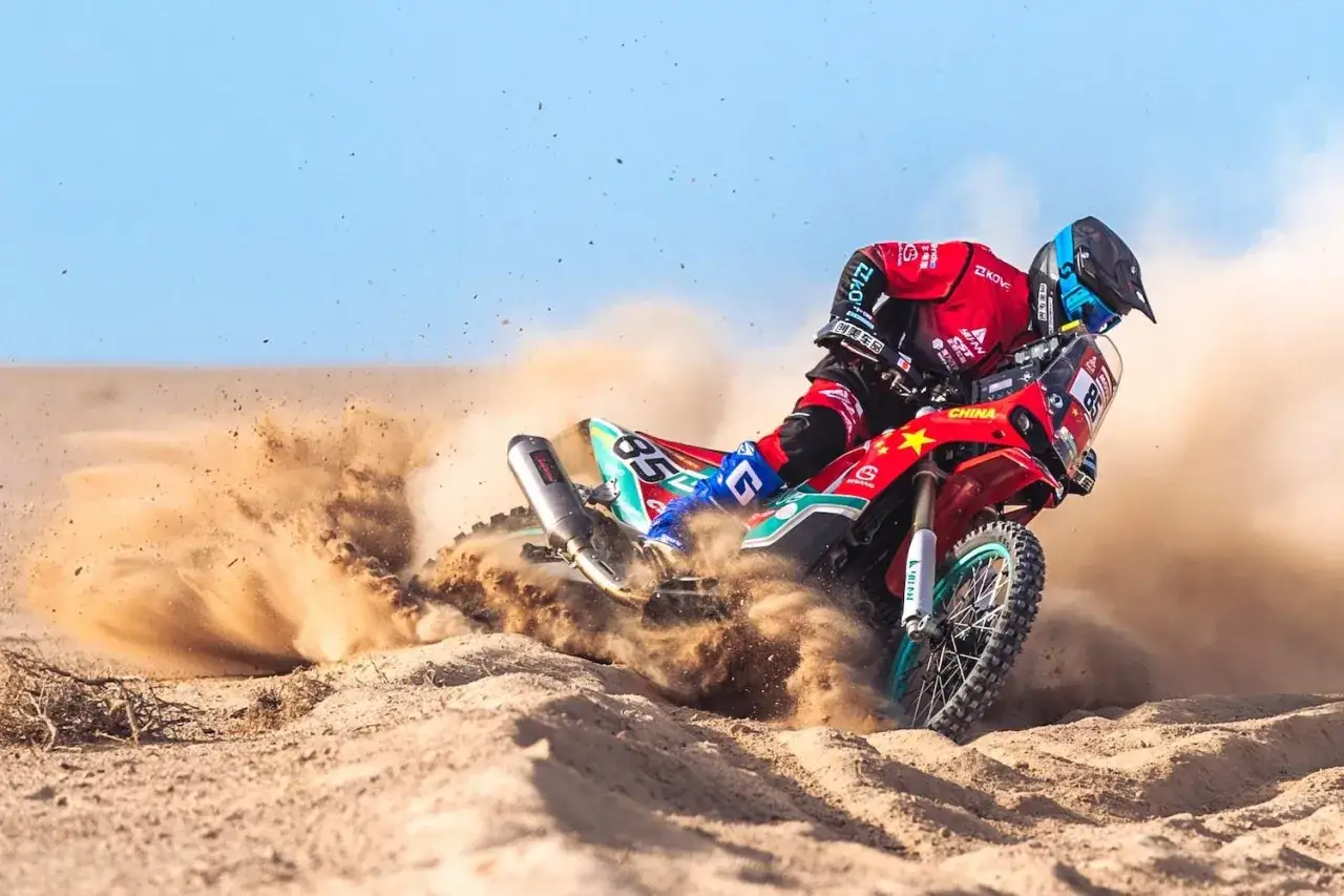 Piloto en moto china dakar levanta arena en carrera desértica.