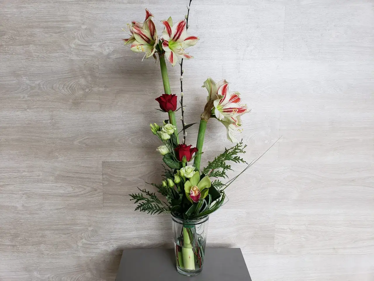 Composition amaryllis avec roses rouges et orchid&eacute;es vertes dans un vase en verre.