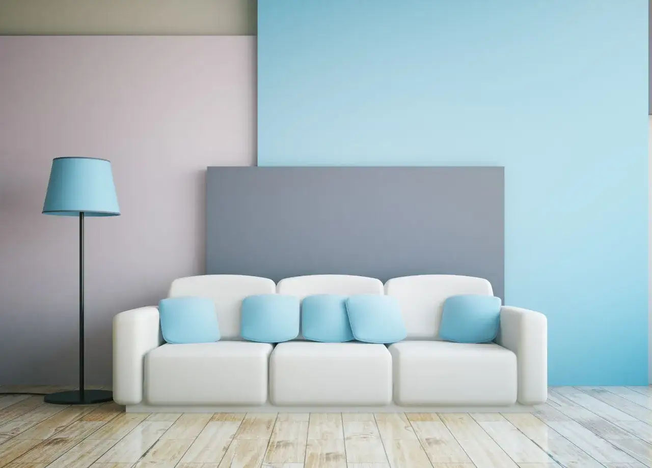 Biała kanapa z poduszkami w kolorze baby blue, obok lampa z abażurem w tym samym odcieniu.