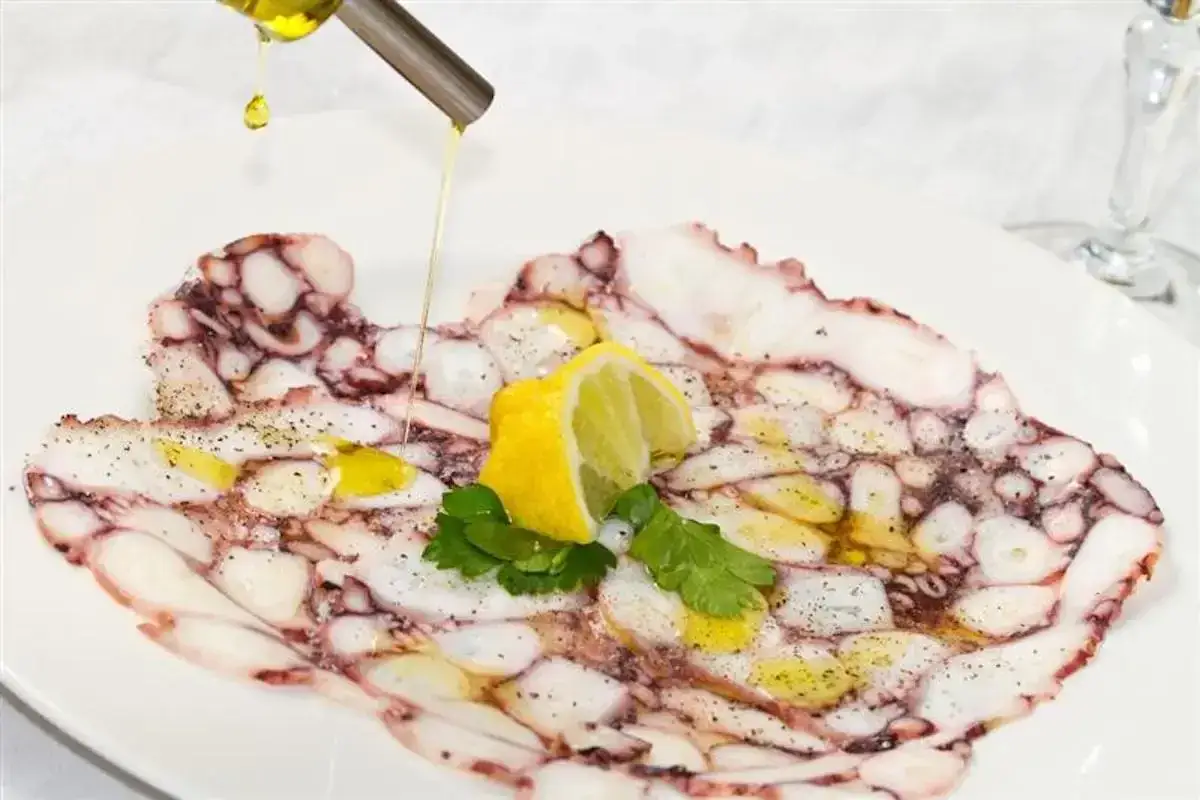 Delicato carpaccio di polpo condito con olio d'oliva, limone e prezzemolo. Un piatto fresco e saporito.