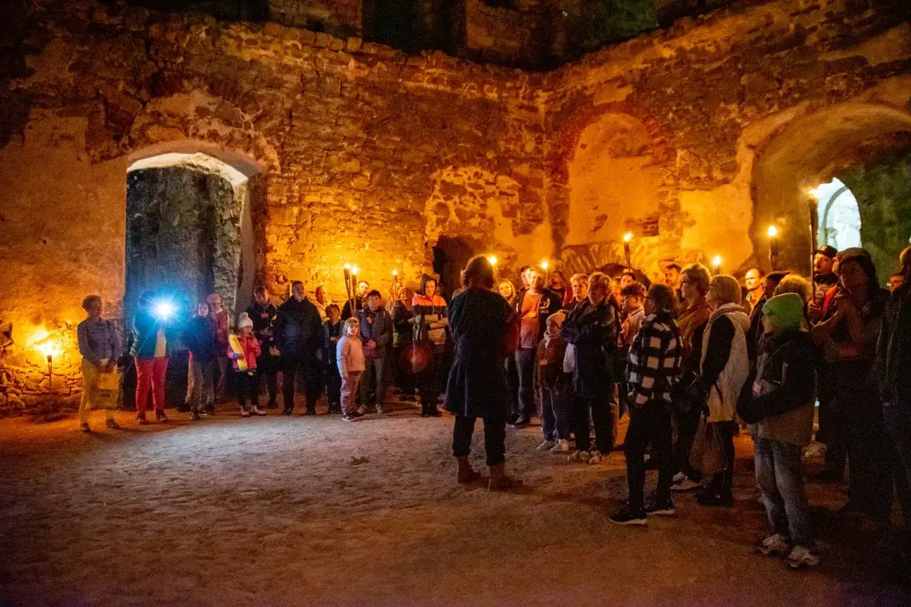 Grupa turystów z pochodniami zwiedza ruiny zamku. Wszyscy mają krzyżtopór bilety, gotowi na nocne odkrycia.