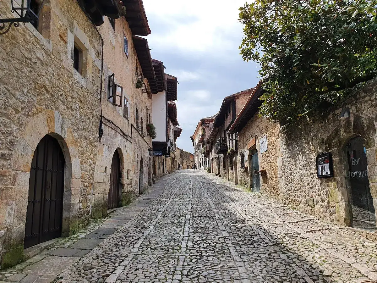 Calle empedrada en Santillana del Mar, Santander, con edificios de piedra y balcones floridos.