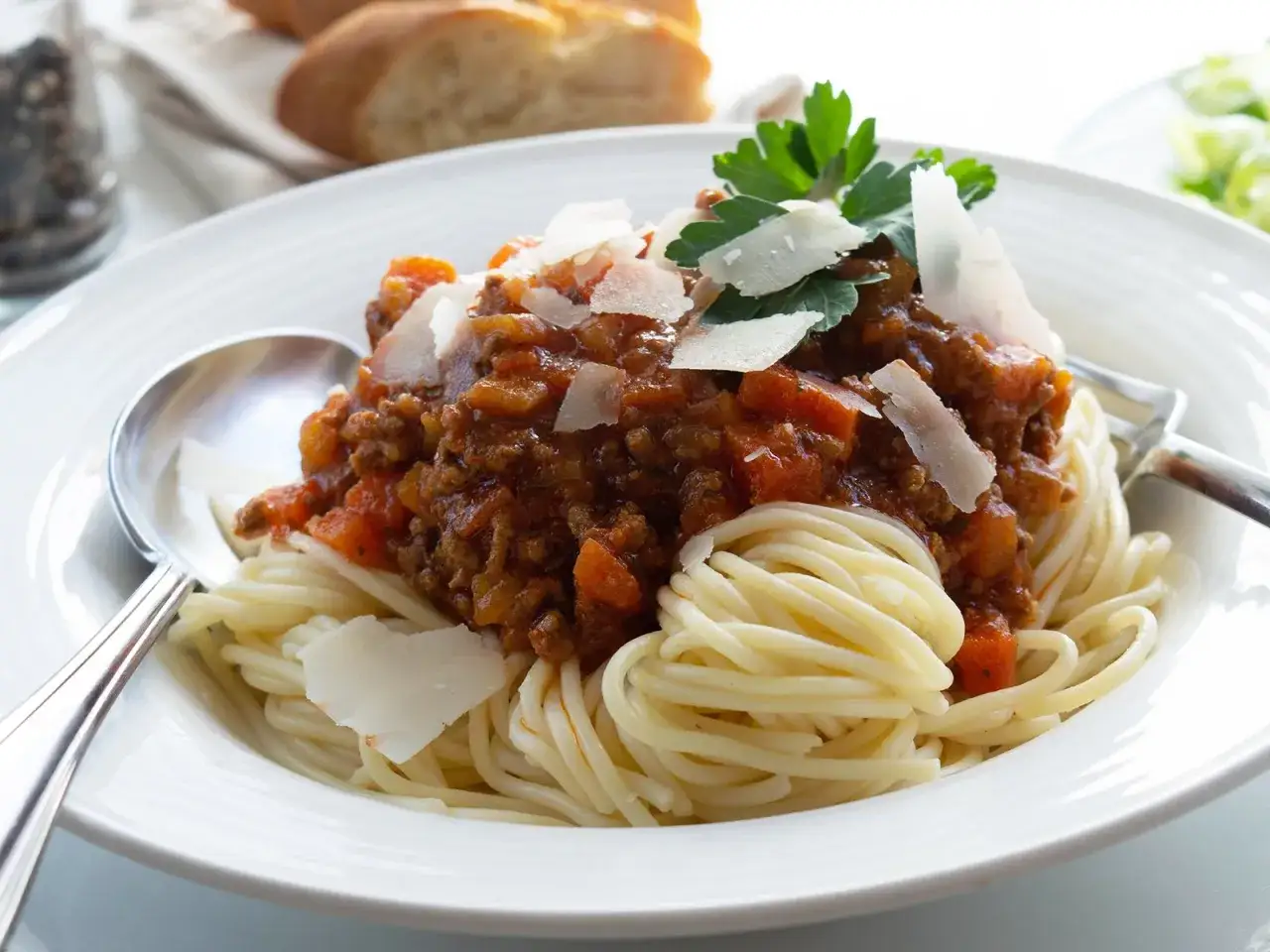 Eine Portion Spaghetti mit einer herzhaften, schnellen Bolognese-Sauce, garniert mit Parmesan und Petersilie. Dazu gibt es Brot.