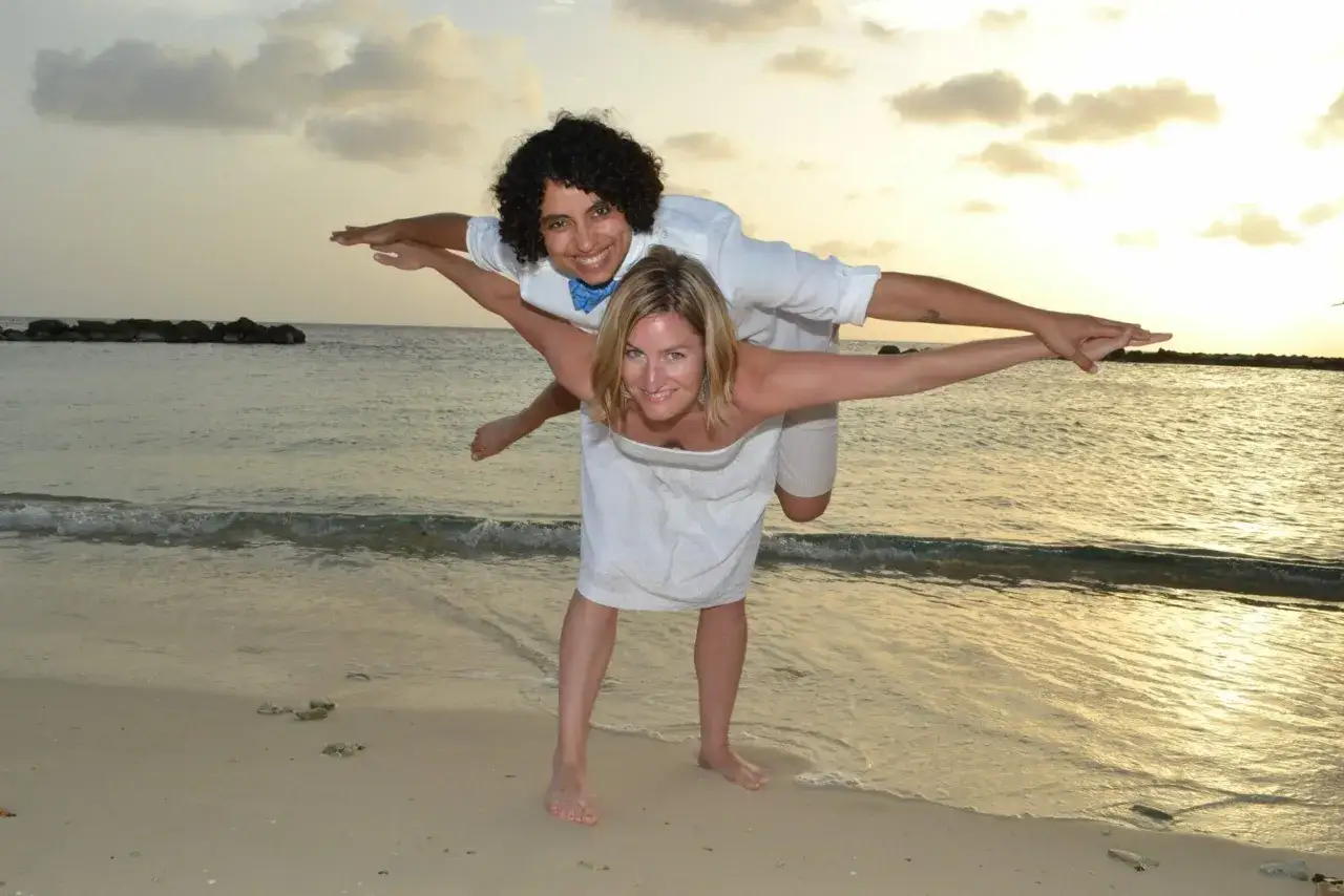 A happy couple enjoys a piggyback ride on a beach in Curacao, a known gay-friendly destination, at sunset.