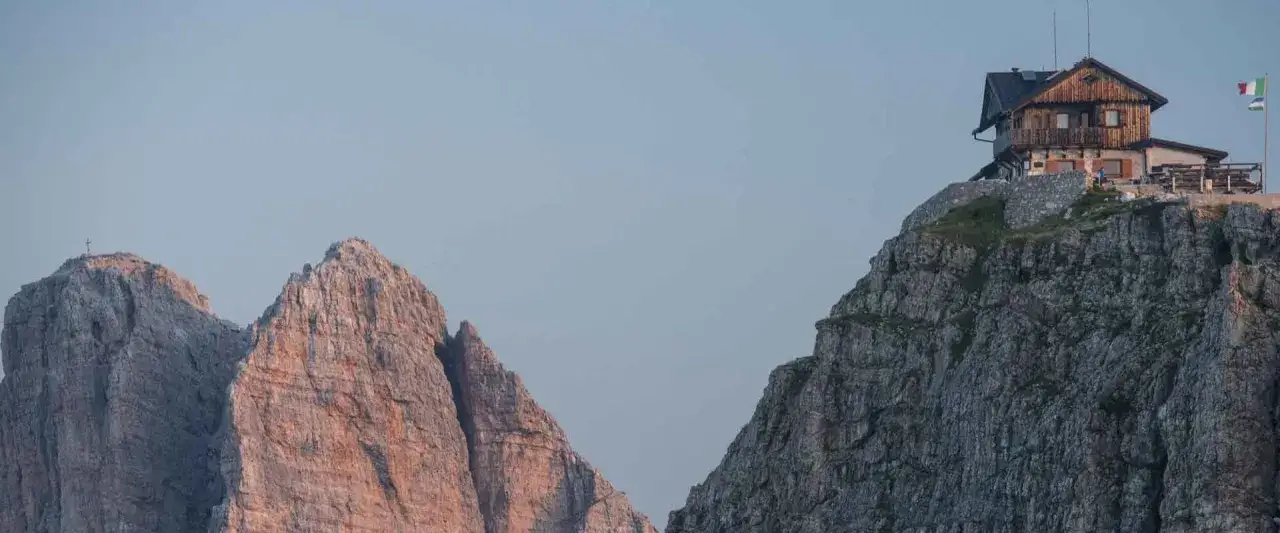 Das Rifugio Nuvolau thront auf einem Felsvorsprung, umgeben von schroffen Berggipfeln unter einem klaren Himmel.