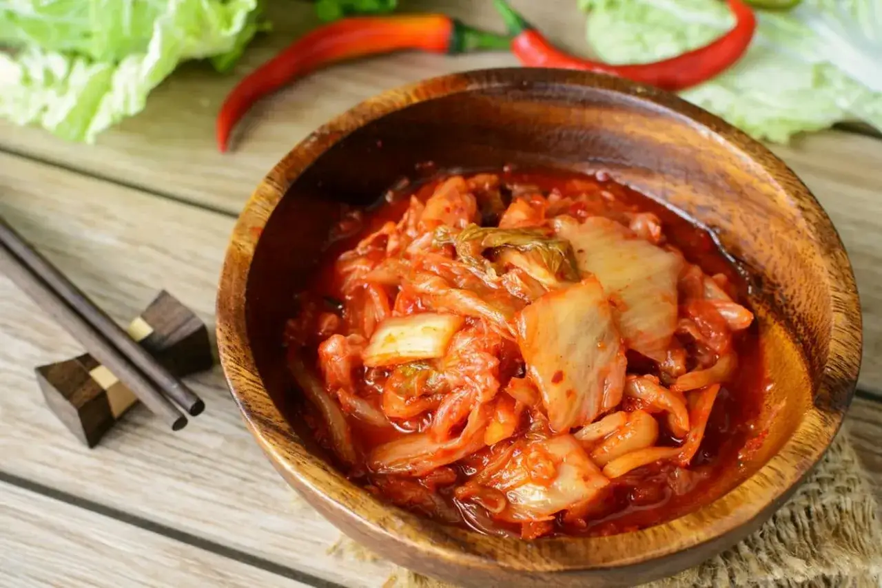 Pikantne kimchi w drewnianej misce, idealne do kuchni koreańskiej przepisy. Obok pałeczki i papryczki chili.