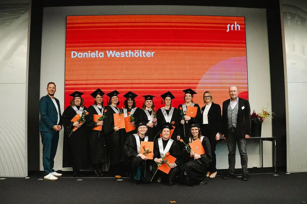 Absolventen feiern ihren Master ohne Bachelor NRW-Abschluss. Sie tragen Talar und Hut und halten Urkunden und Rosen.