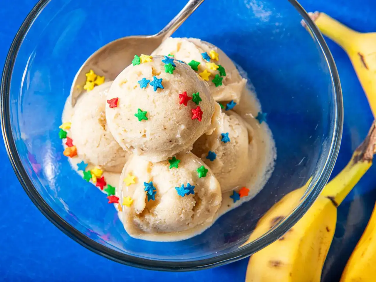 Nicecream in einer blauen Sch&uuml;ssel, garniert mit bunten Sternen. Bananen liegen daneben.