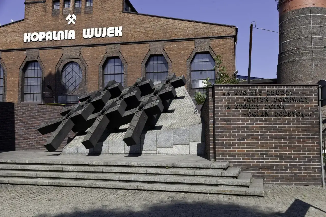 Pomnik upamiętniający pacyfikację kopalni Wujek. Monumentalna rzeźba na tle ceglanego budynku kopalni.