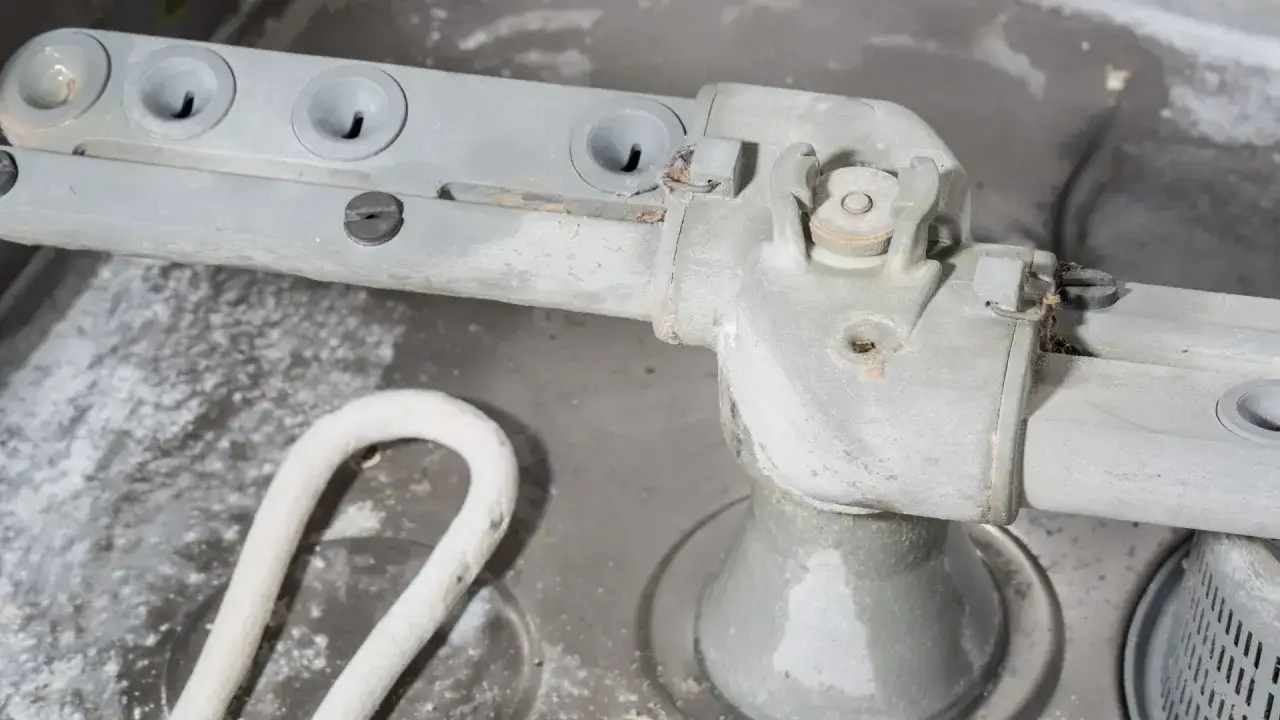 Bras rotatif d'un lave-vaisselle encrass&eacute; par le calcaire. Des d&eacute;p&ocirc;ts blancs recouvrent le m&eacute;tal et les &eacute;l&eacute;ments chauffants.