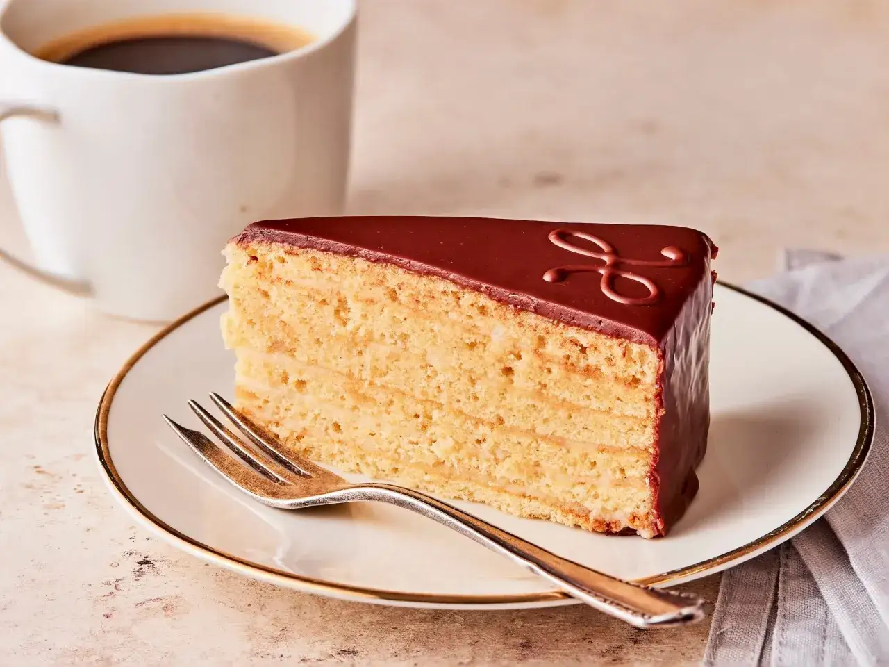Ein St&uuml;ck Schokoladenkuchen mit vielen Schichten, perfekt f&uuml;r ein Herrentorte Rezept. Daneben eine Tasse Kaffee.