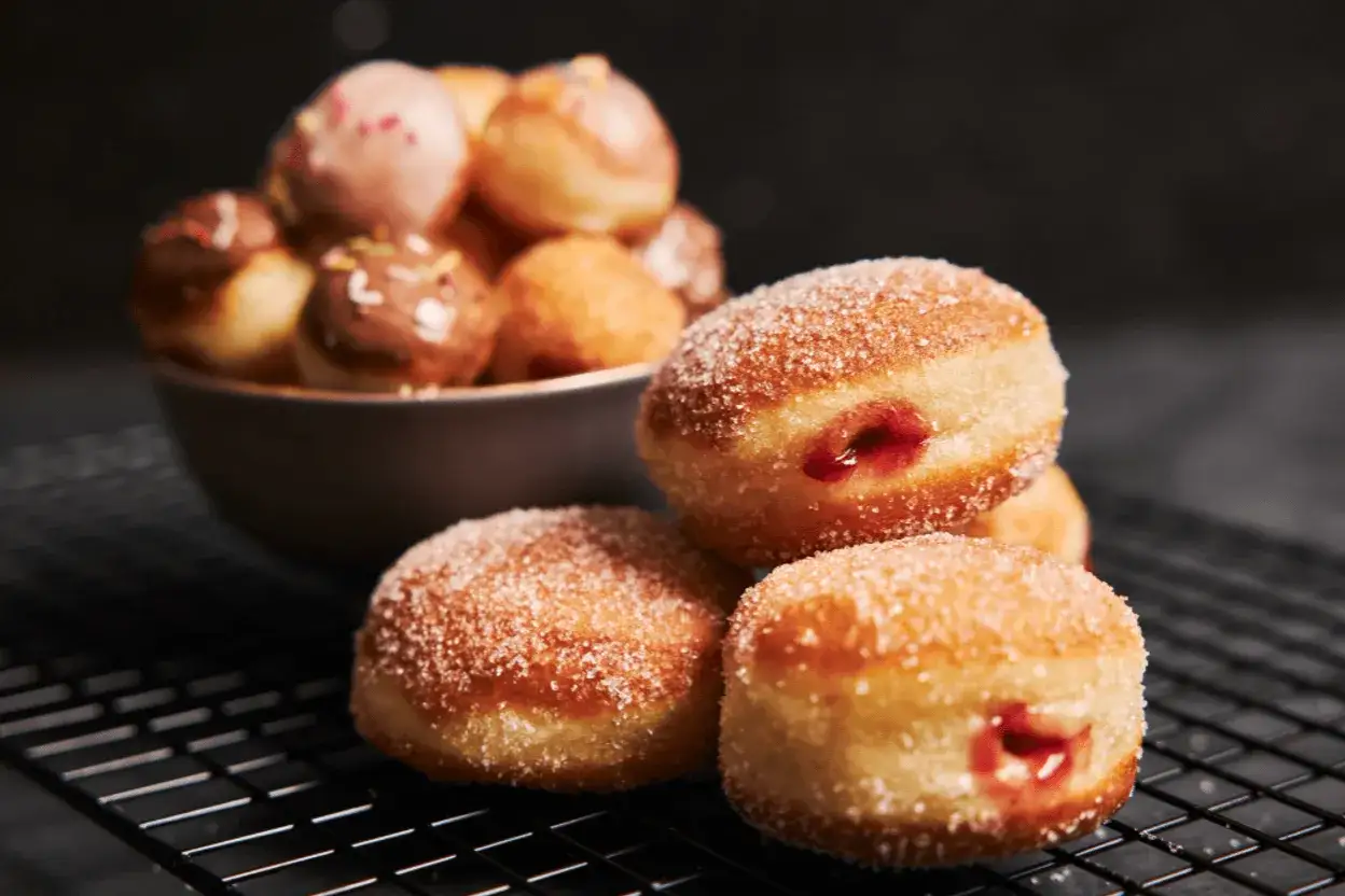 Pączki z dżemem i cukrem na ruszcie, a w tle miska z mini pączkami. Dowiedz się, jak przechowywać pączki, by były świeże.