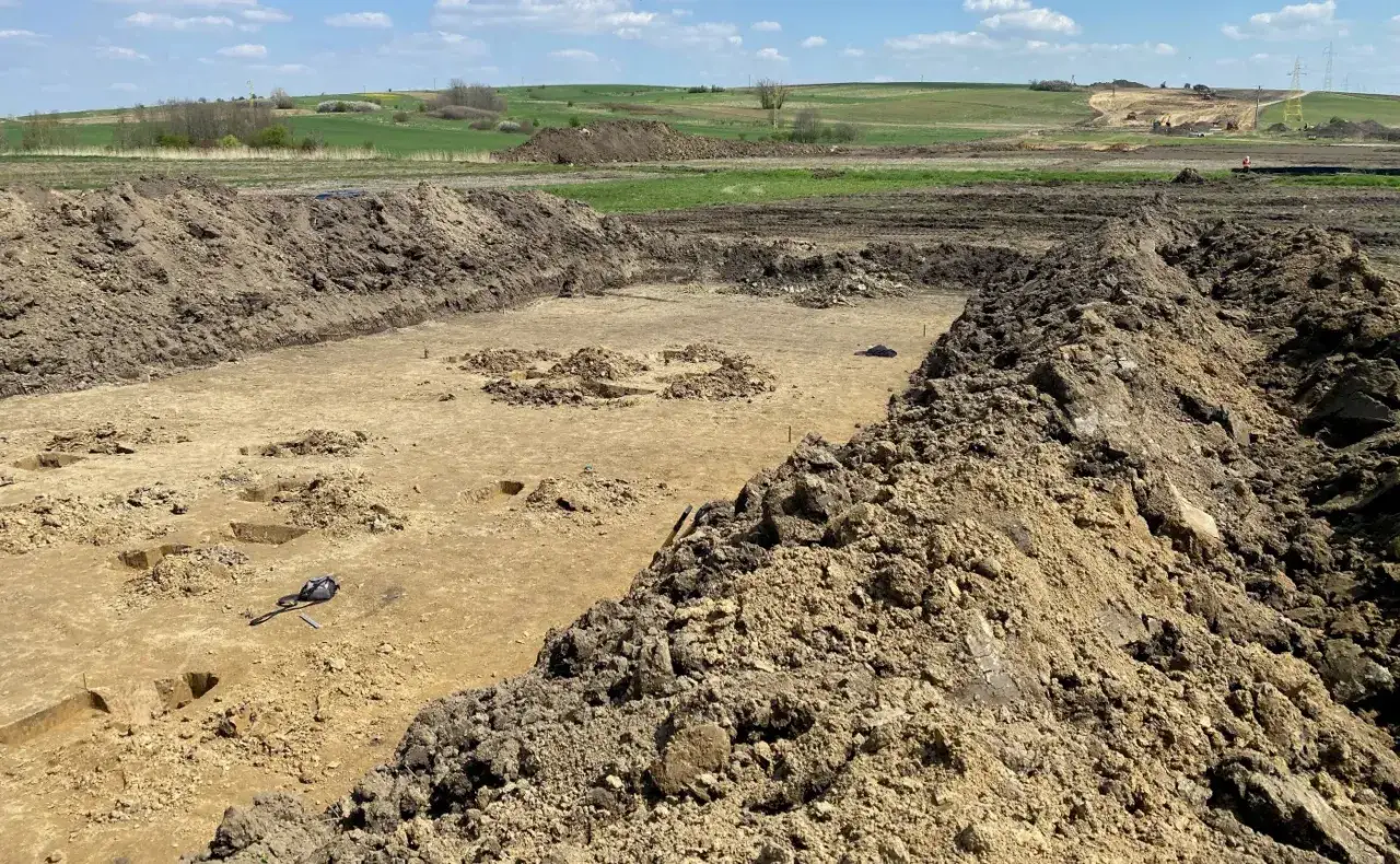 Wykopalisko archeologiczne z widocznym zarysem budowli i ziemią usypaną na brzegach. Zrid.