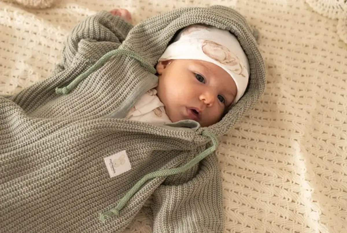 Malutkie dziecko w czapce z kr&oacute;liczkiem i szarym pajacyku na wyjście ze szpitala, otulone w miękki kocyk.