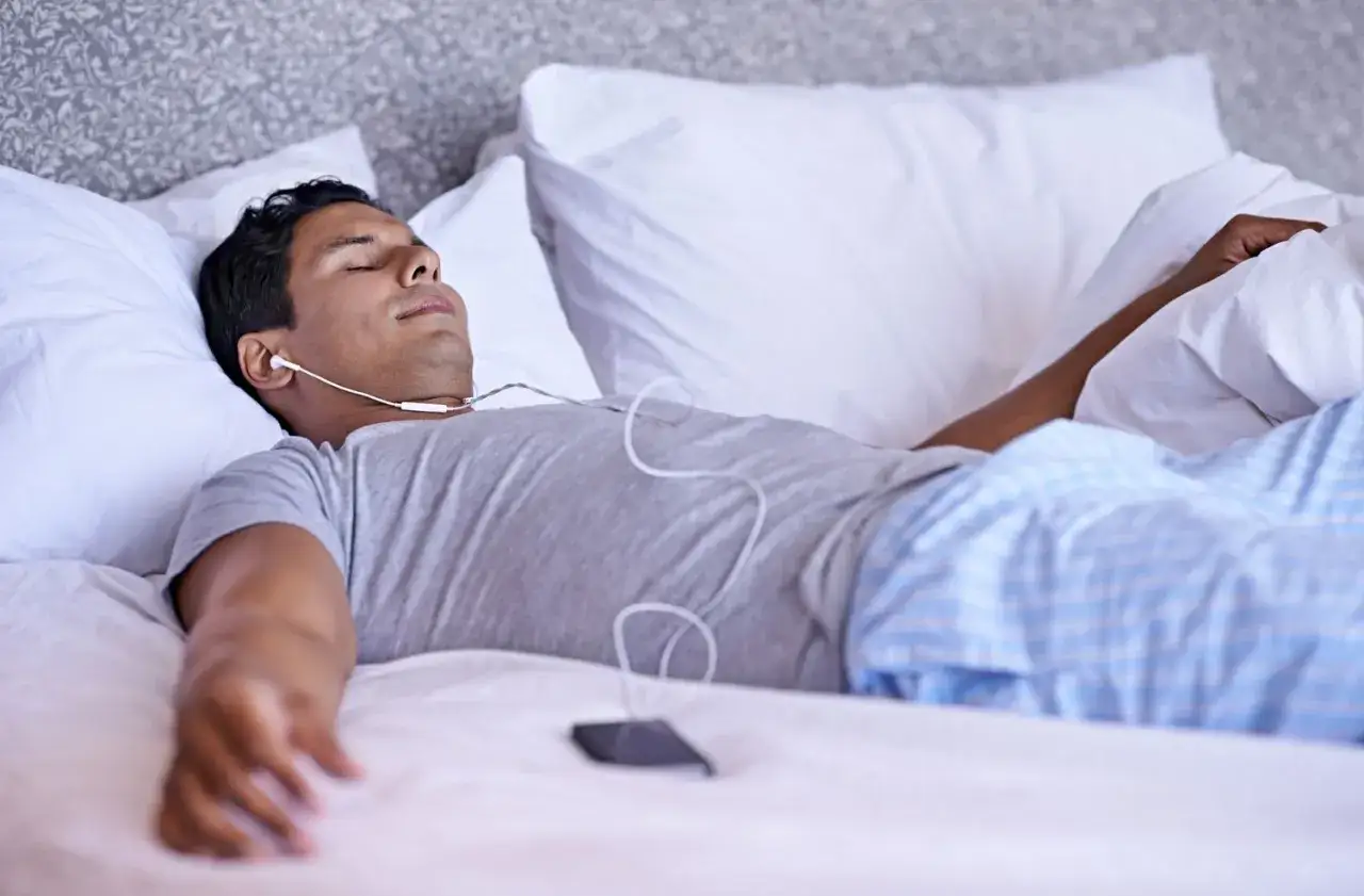 Uomo rilassato a letto con auricolari, ascolta musica o meditazione per esercizi per dormire.
