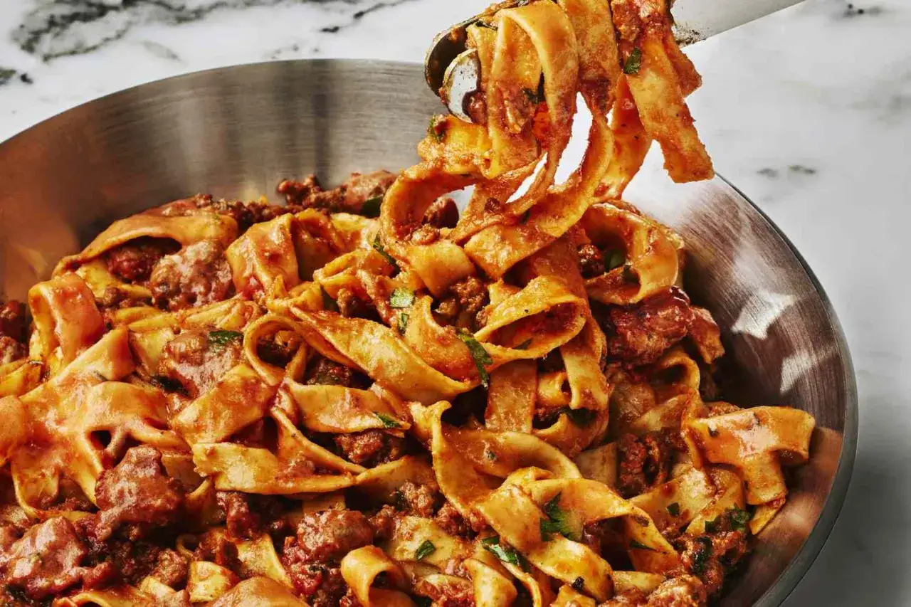 Breite Bandnudeln mit einer herzhaften Sauce aus zerkleinerter Salsiccia-Wurst und Kr&auml;utern in einer Edelstahlsch&uuml;ssel.