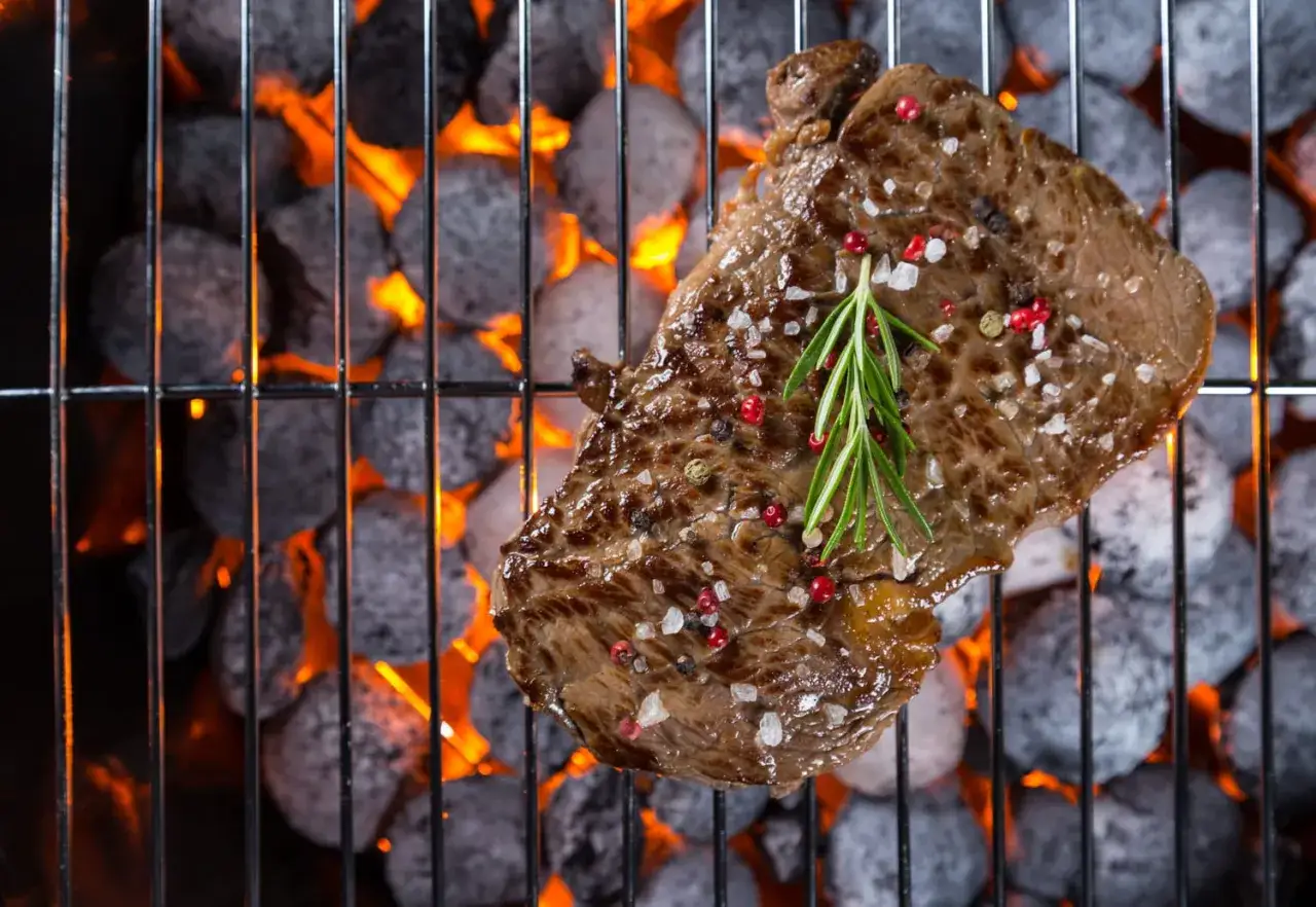 Un succulent morceau de viande grillée, assaisonné de gros sel et de poivre rose, avec une branche de romarin, cuit sur des braises ardentes.