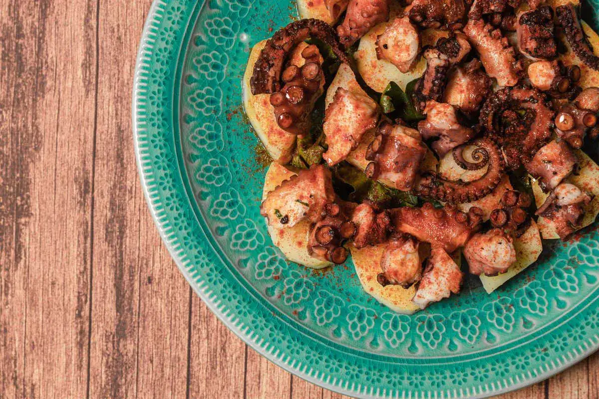 Piatto di polpo alla gallega su patate, condito con paprika e olio d'oliva, servito su un piatto decorato.