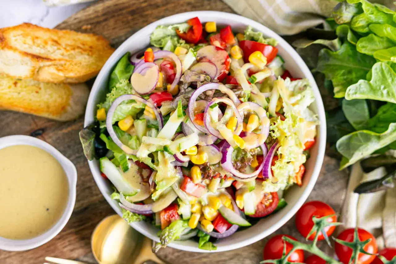 Ein bunter gemischter Salat mit knackigem Salat, Tomaten, Gurken, Mais und roten Zwiebeln, serviert mit Dressing und geröstetem Brot.