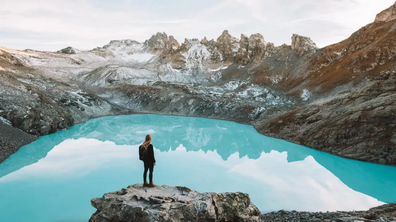 Une randonneuse admire la beauté d'un lac suisse aux eaux turquoise, entouré de montagnes enneigées.