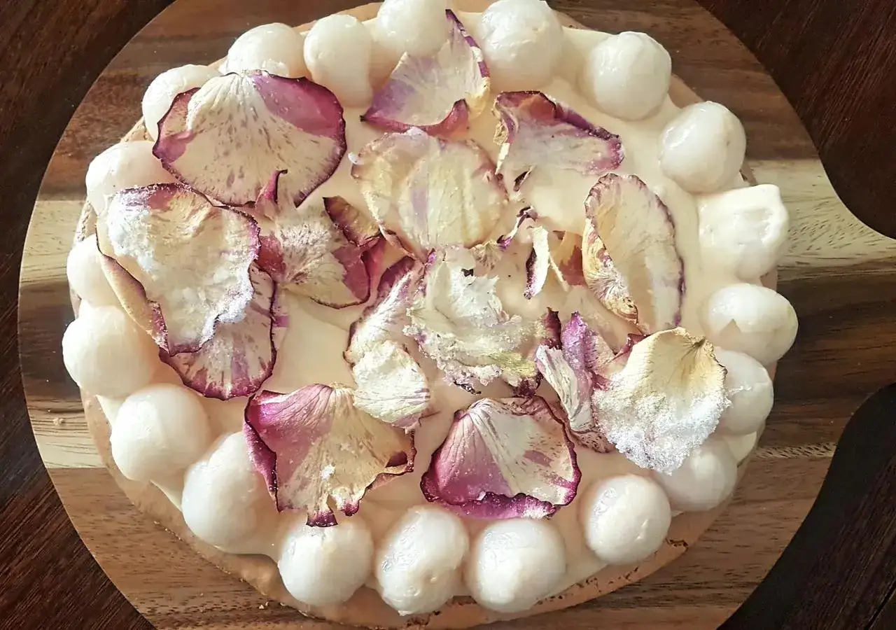 Okrągły tort udekorowany kremem, płatkami róż i kuleczkami przypominającymi lychee.