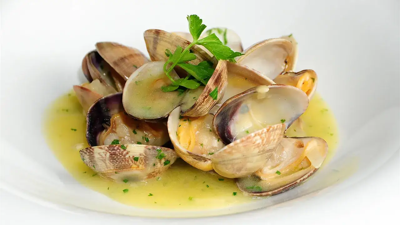 Deliciosas almejas en salsa verde, con perejil fresco, servidas en un plato blanco.