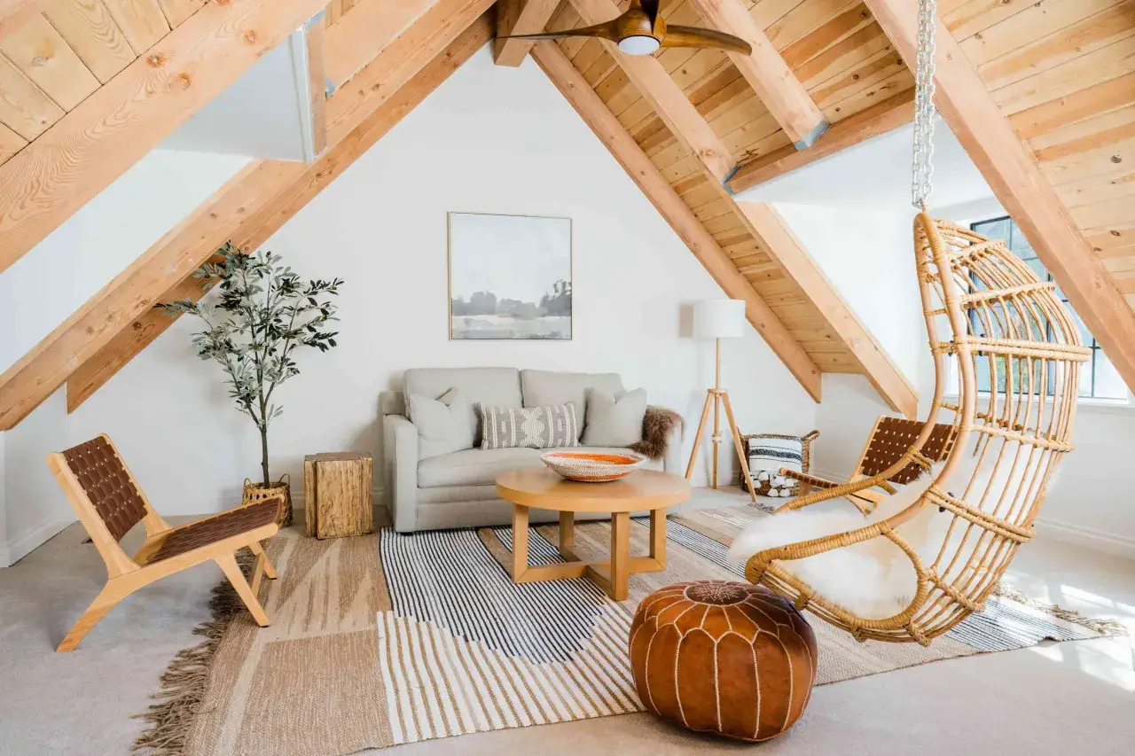Un salon cosy aménagé sous les combles, avec des poutres apparentes, un fauteuil suspendu en rotin et une décoration bohème. Ce grenier est un havre de paix.