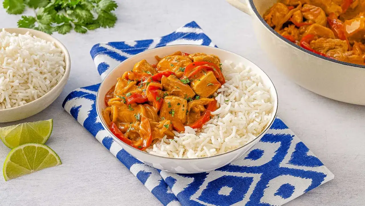Un invitante pollo al curry con latte di cocco, servito con riso basmati e spicchi di lime.
