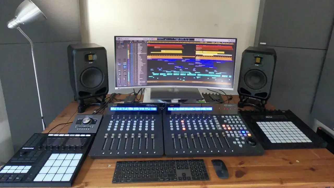 Studio d'enregistrement avec écran large affichant une piste audio, deux enceintes, des consoles de mixage et des pads de batterie pour une expérience de musique stéréo immersive.