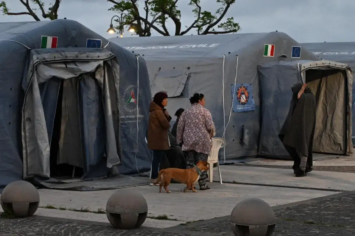 Ludzie i pies czekają przed namiotami Protezione Civile we Włoszech po trzęsieniu ziemi.