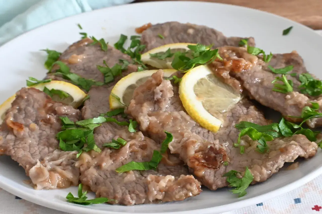 Scaloppine al limone su un piatto bianco, guarnite con fette di limone e prezzemolo fresco.