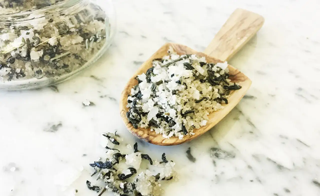 A wooden scoop holds a mixture of coarse salt and dried herbs, perfect for a best natural foot soak.