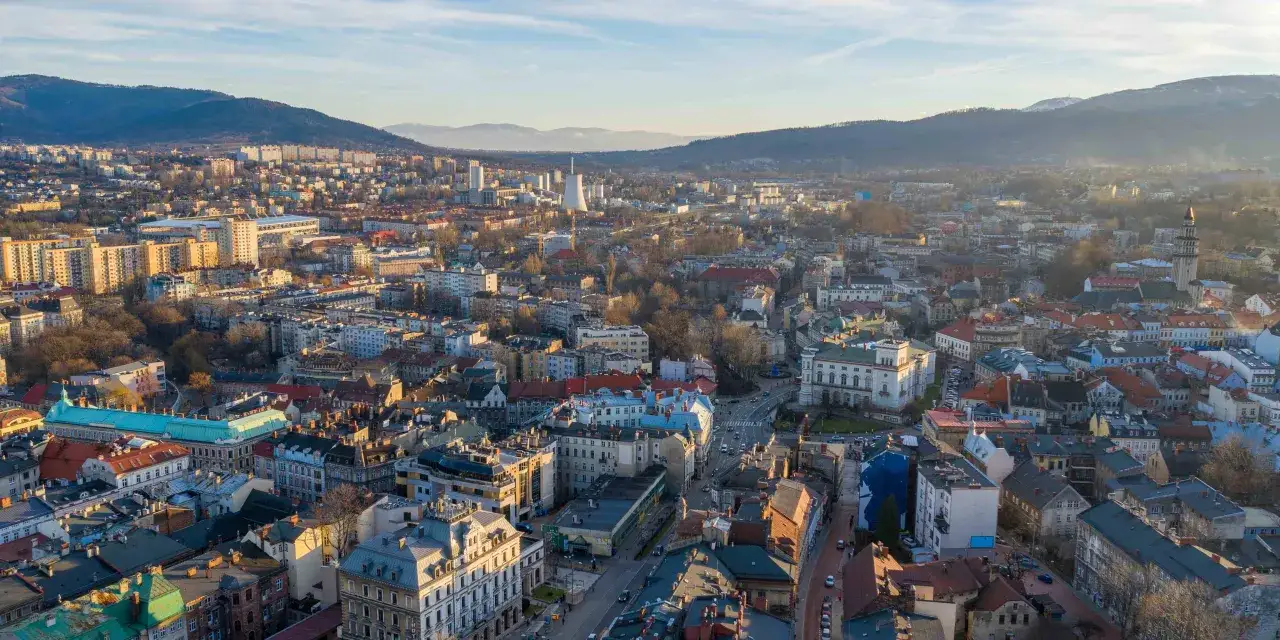 Widok na miasto z lotu ptaka, ukazujący bielsko-biała atrakcje, w tym zabytkowe kamienice i g&oacute;ry w tle.