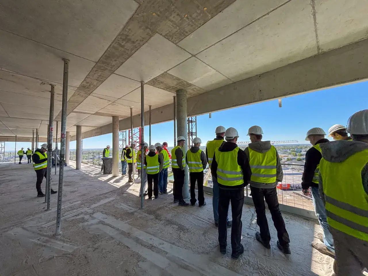 Bauingenieure im Studium in NRW besichtigen eine Baustelle. Sie tragen Warnwesten und Helme.
