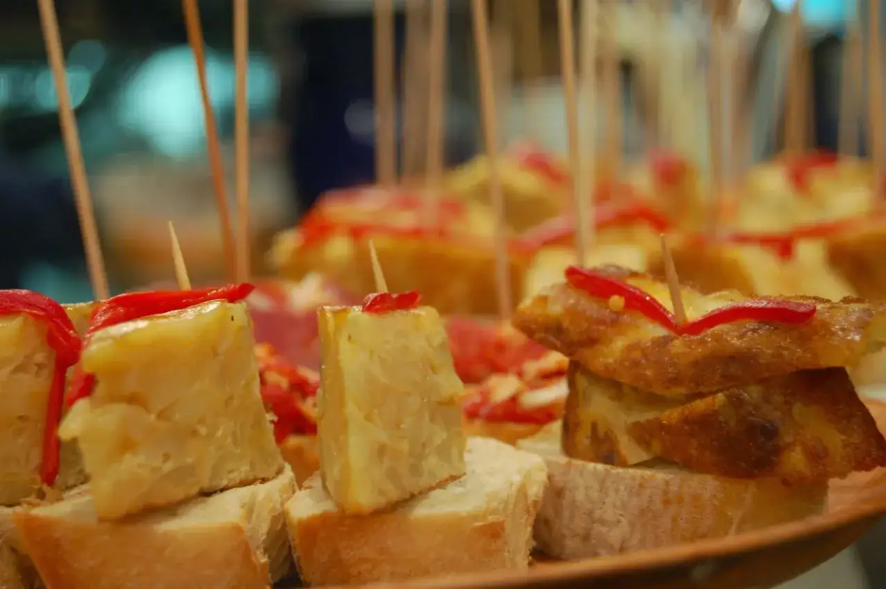 Pyszne pinchos z tortillą ziemniaczaną i papryką, nadziane wykałaczkami, kuszą na talerzu.