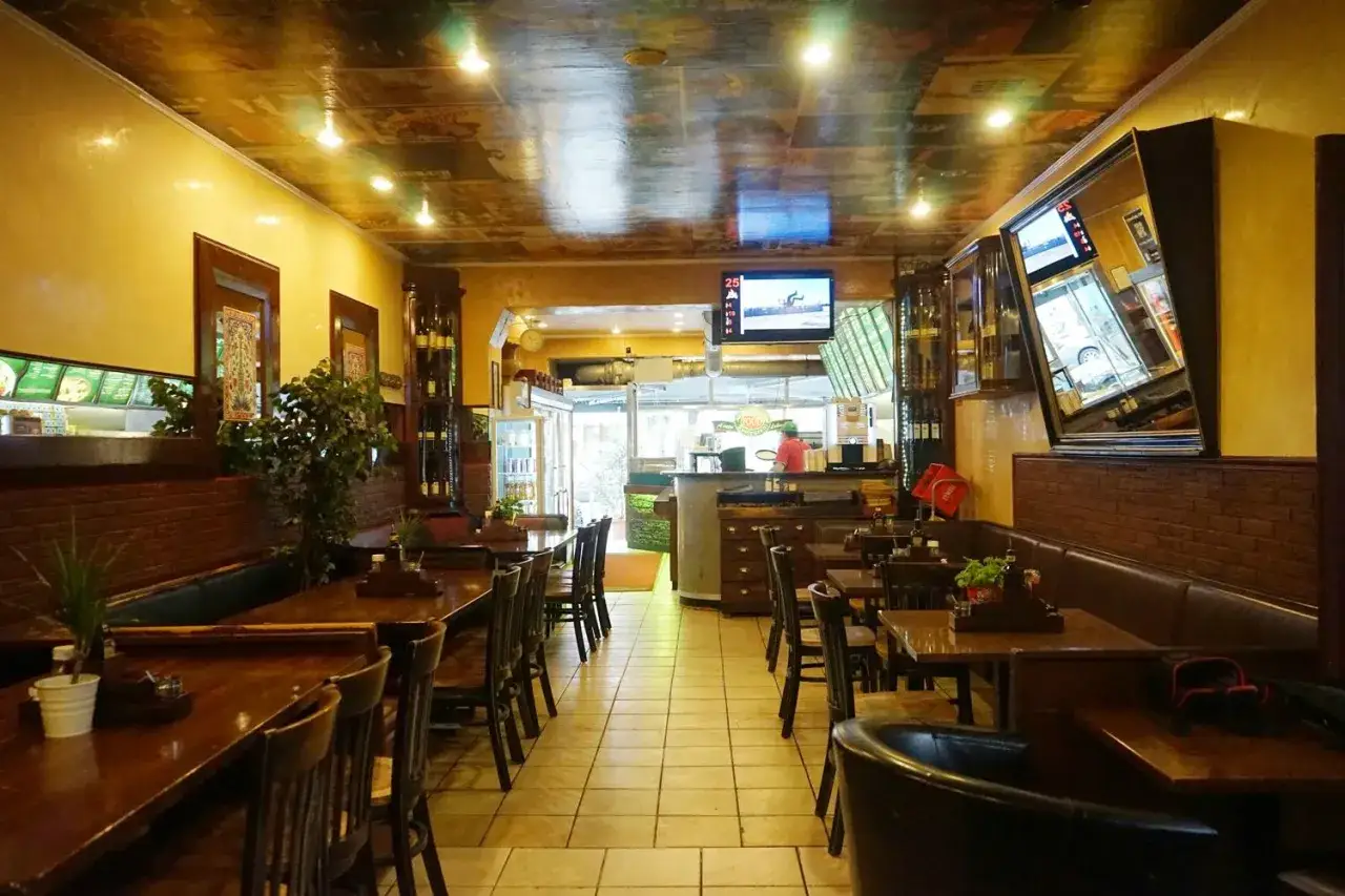 Gem&uuml;tliches Restaurant mit Holztischen und braunen Lederb&auml;nken. An der Wand h&auml;ngen Spiegel und Regale mit Flaschen. Die Decke ist mit Bildern dekoriert. i due forni l&auml;dt zum Verweilen ein.