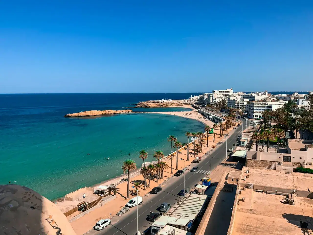 Vue d'une ville côtière tunisienne avec une plage de sable, des palmiers et des bâtiments blancs. Parfait pour savoir que faire en Tunisie !
