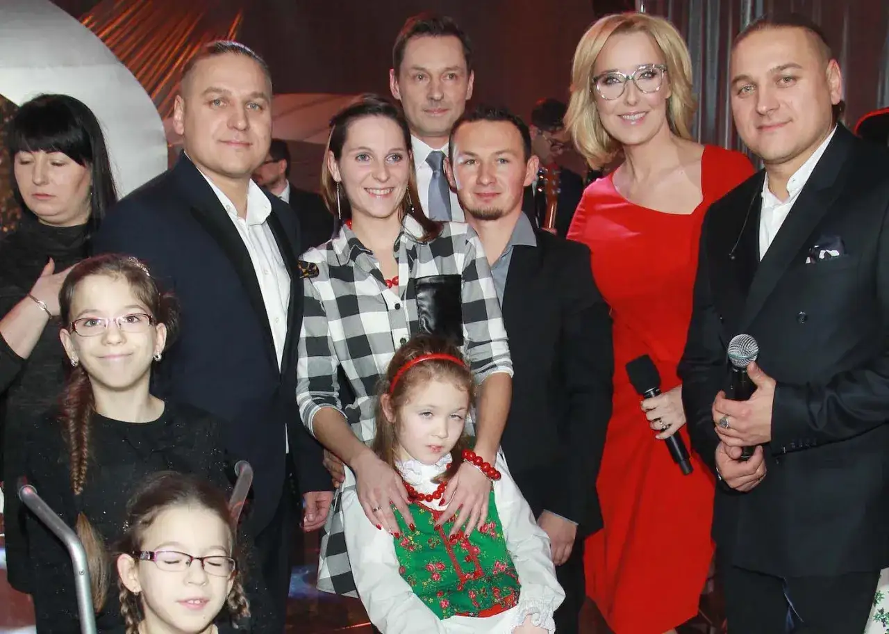 Grupa osób na scenie, w tym dwie dziewczynki. Jedna z nich, w ludowym stroju, wygląda na córkę, która ma golce.