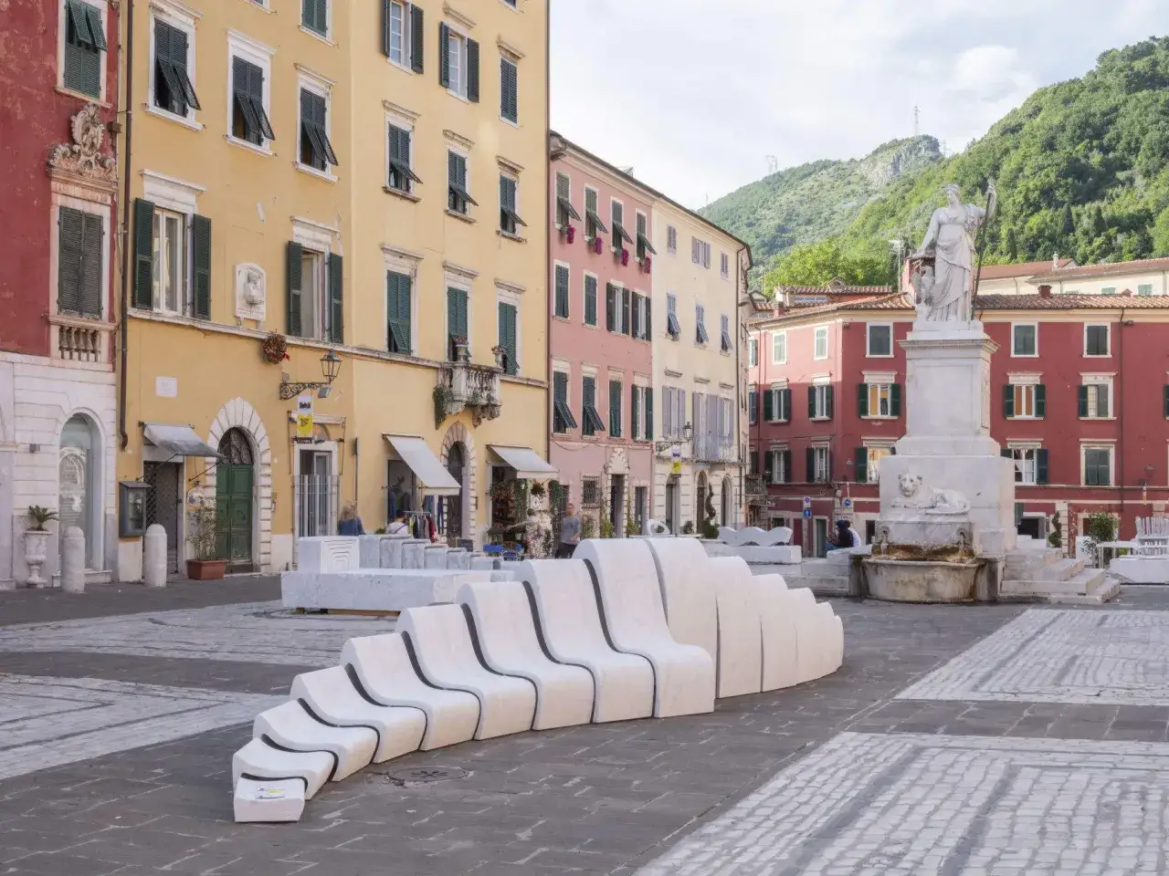 Piazza nel carrara centro storico con sculture moderne in marmo e palazzi colorati.