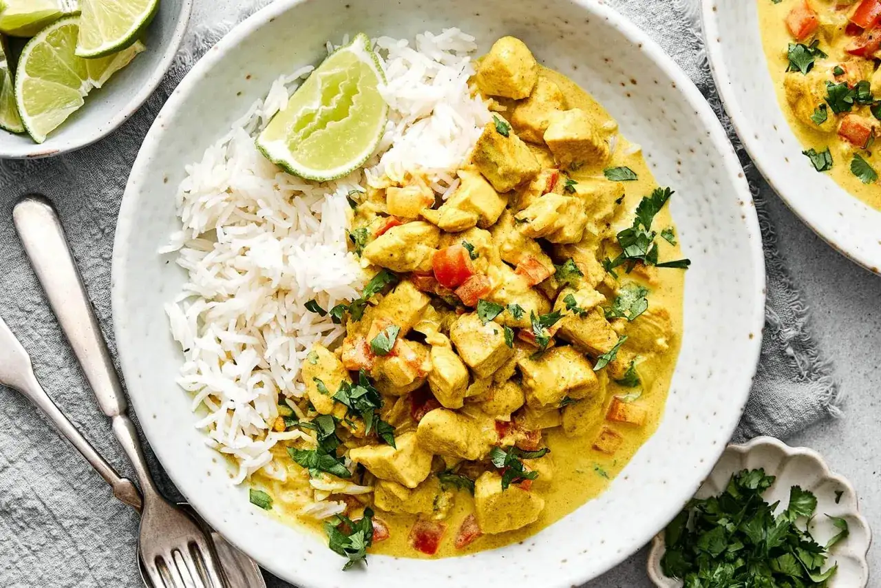 Ein cremiger H&auml;hnchen-Thai-Curry mit Reis, garniert mit frischer Koriander und Limettenspalten.
