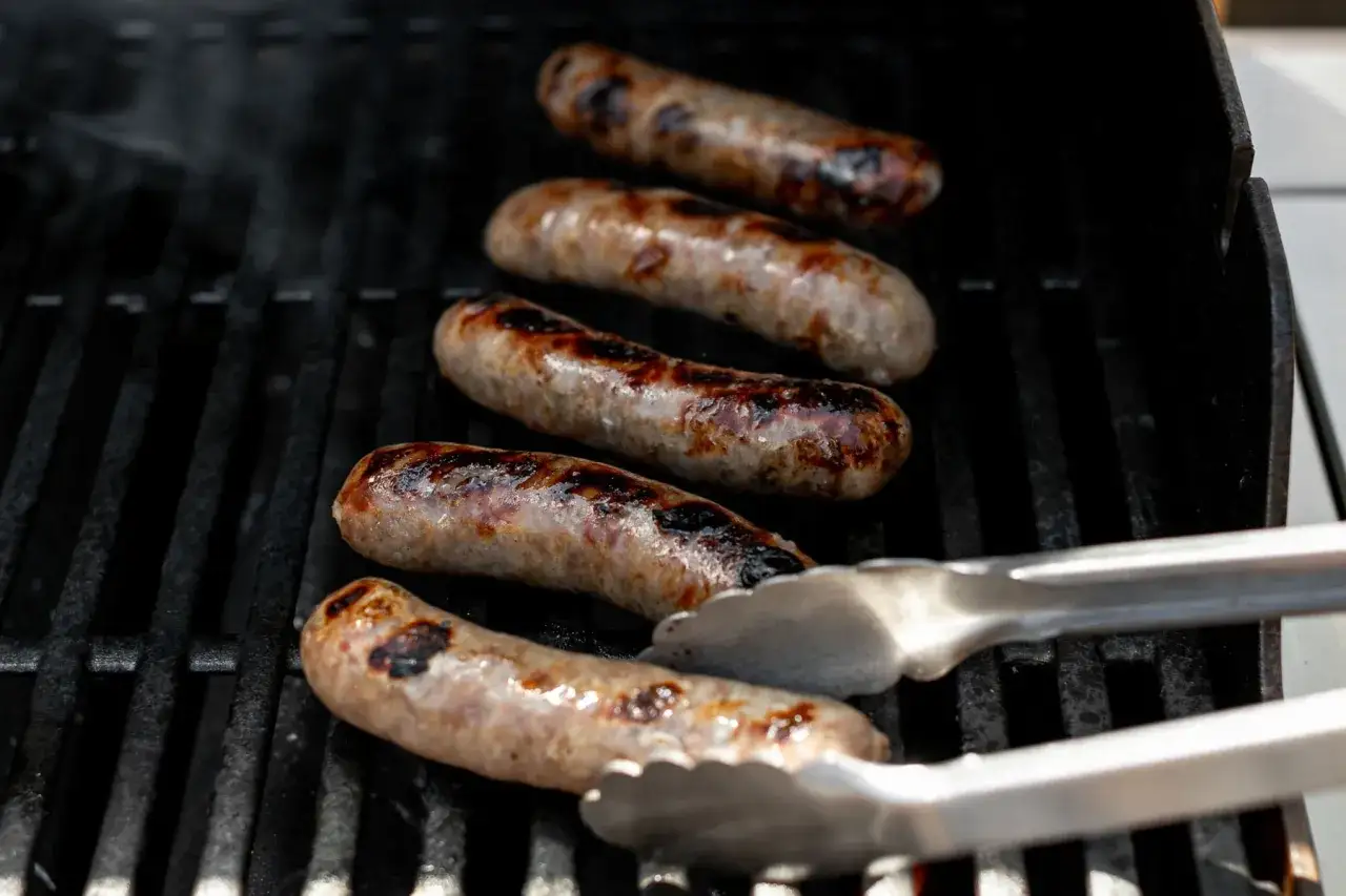 Fem saftiga korvar grillas på en kolgrill. Röken stiger och ger en härlig doft.
