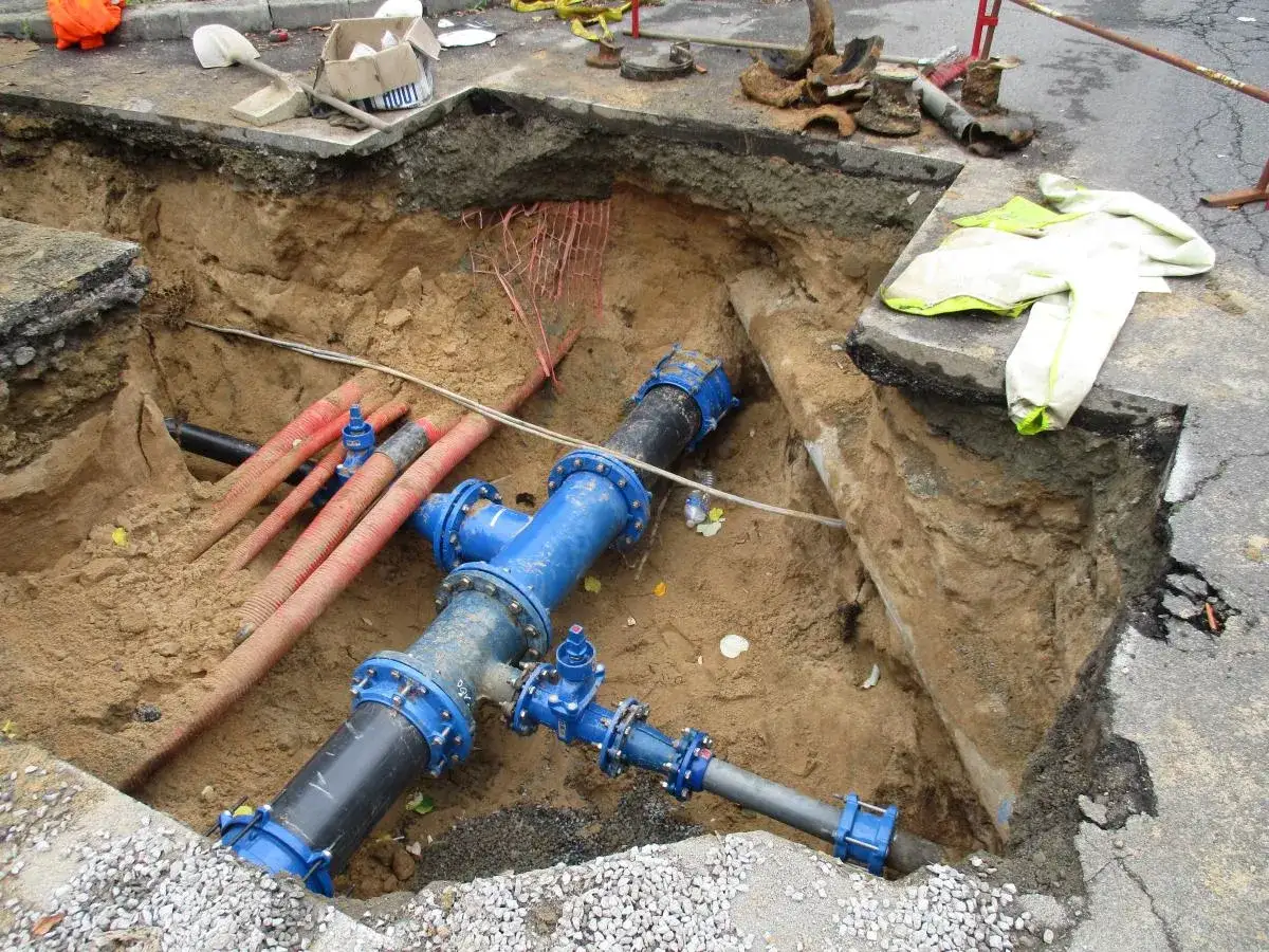 Travaux de voirie : une canalisation d'eaux us&eacute;es enterr&eacute;e est en cours de remplacement. Des tuyaux bleus imposants et des conduits rouges sont visibles dans la tranch&eacute;e.