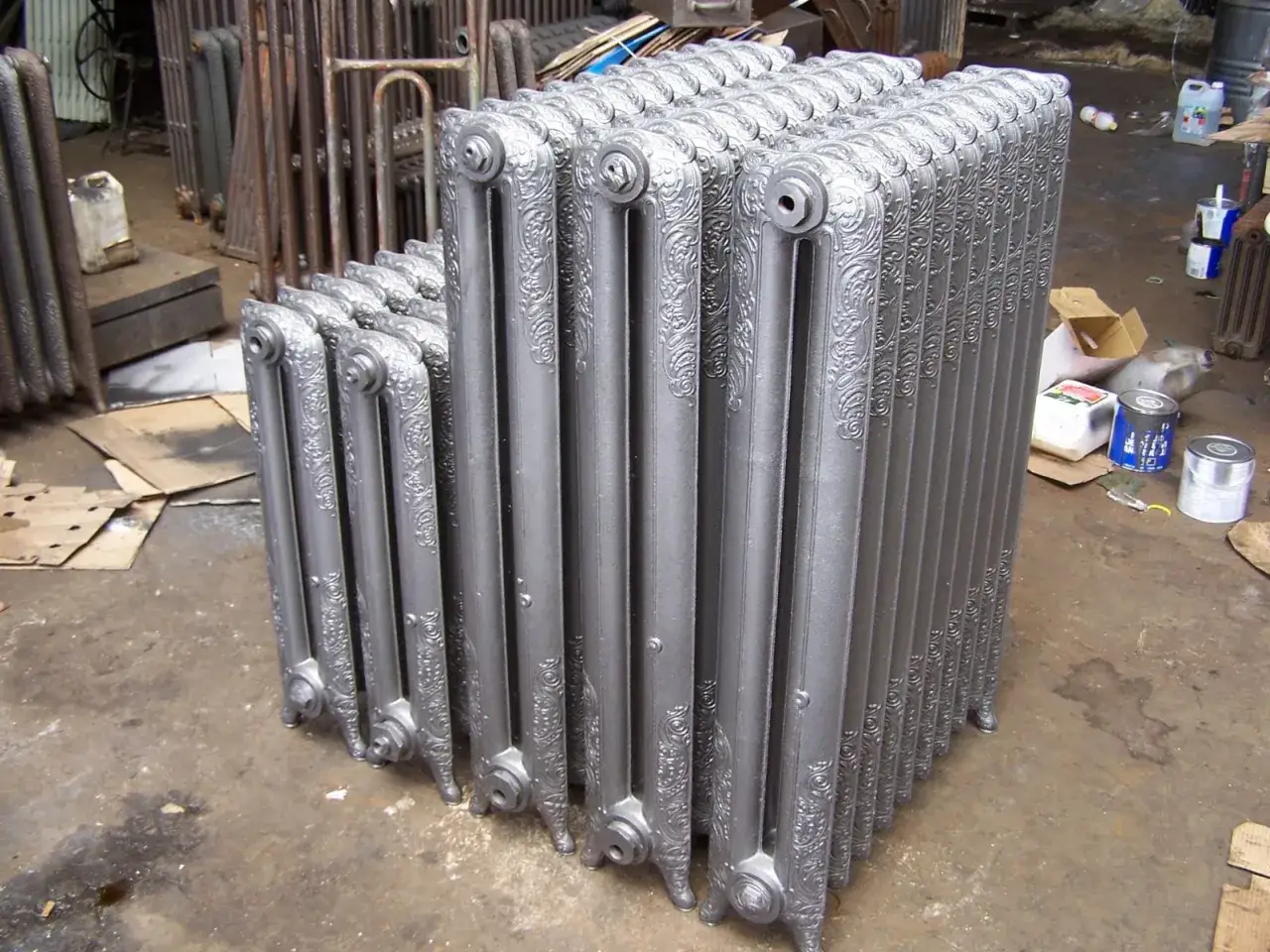 Une rangée de radiateurs en fonte argentés, prêts à être installés. Ces pièces classiques permettent de reconnaître radiateur haute température et apportent une touche d'élégance.